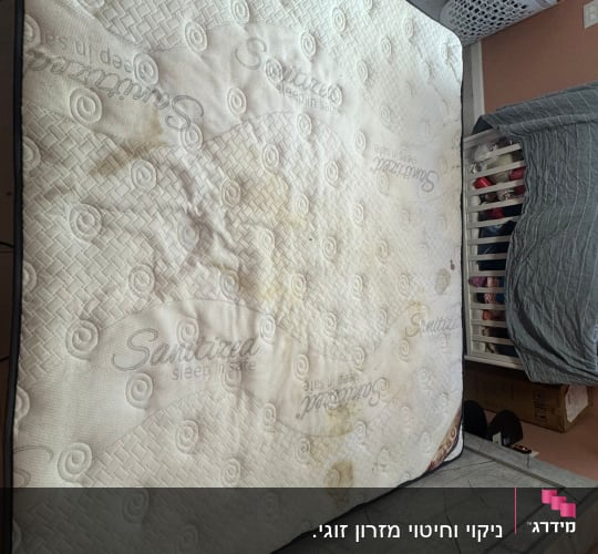 מזרן עם כתמים על הרצפה ליד סל כביסה
